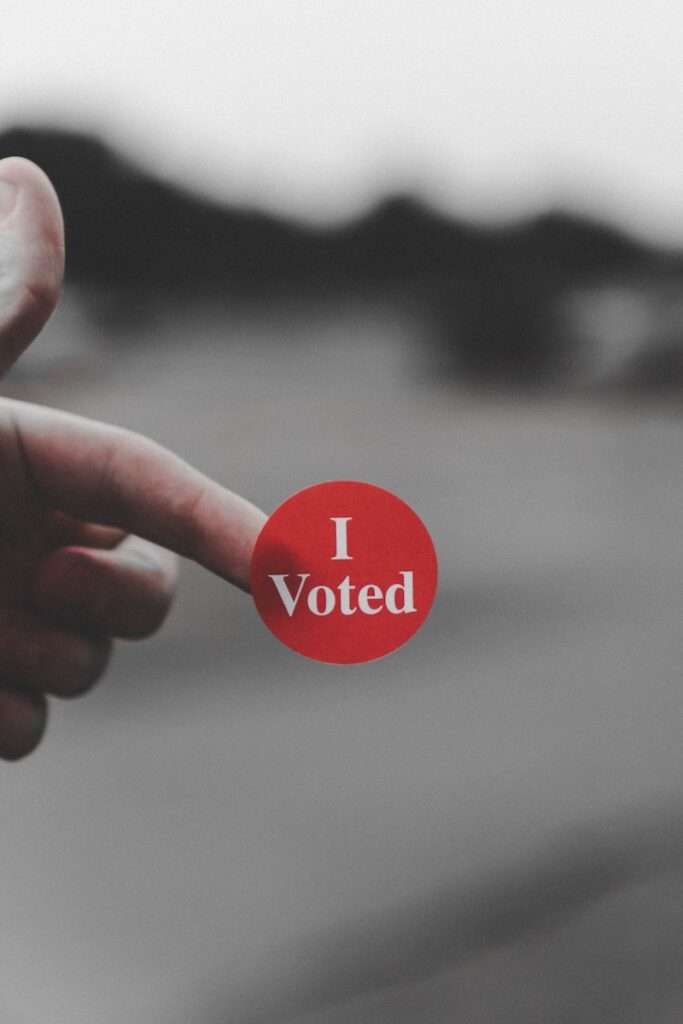 a hand holding a red button that says i vote